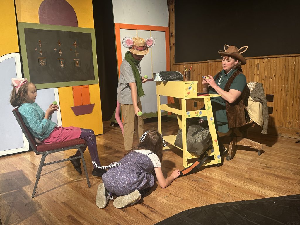 Three children and an adult act out a scene dressed as a cat, dog, mouse and fox.