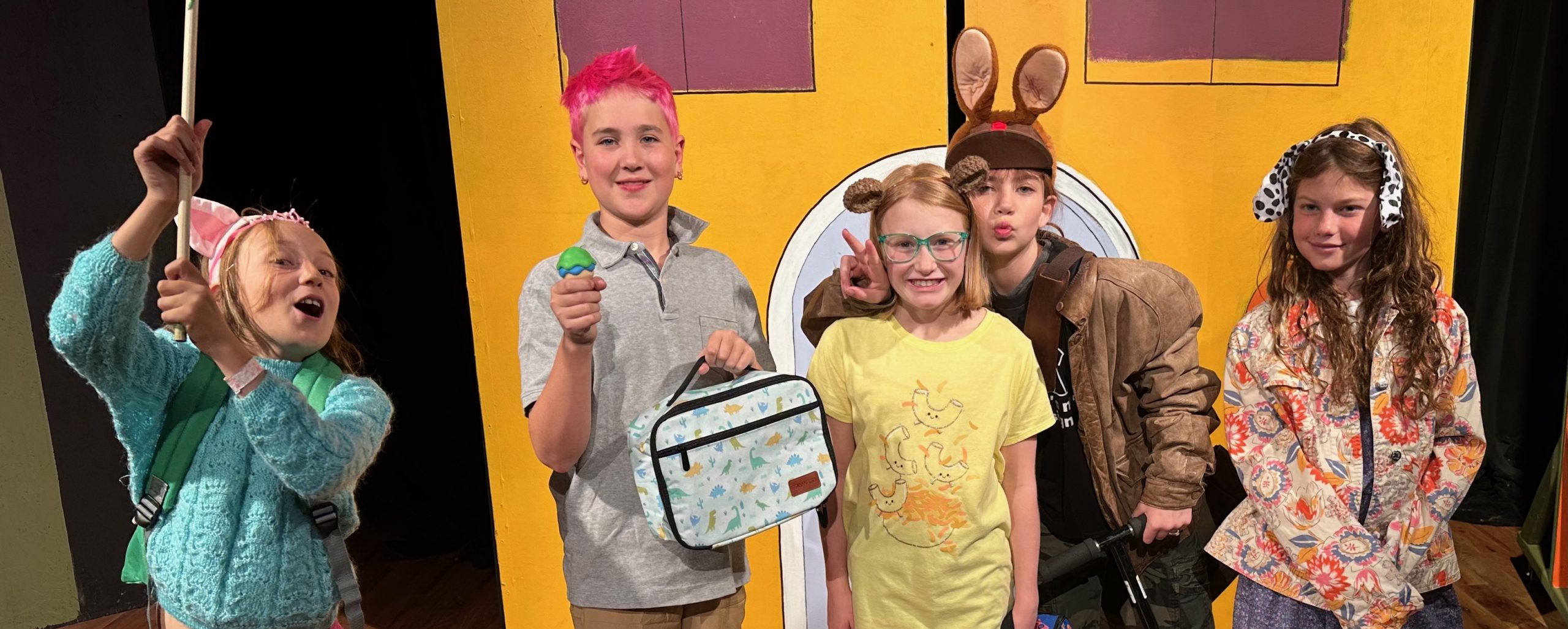 Five child actors strike poses on stage.