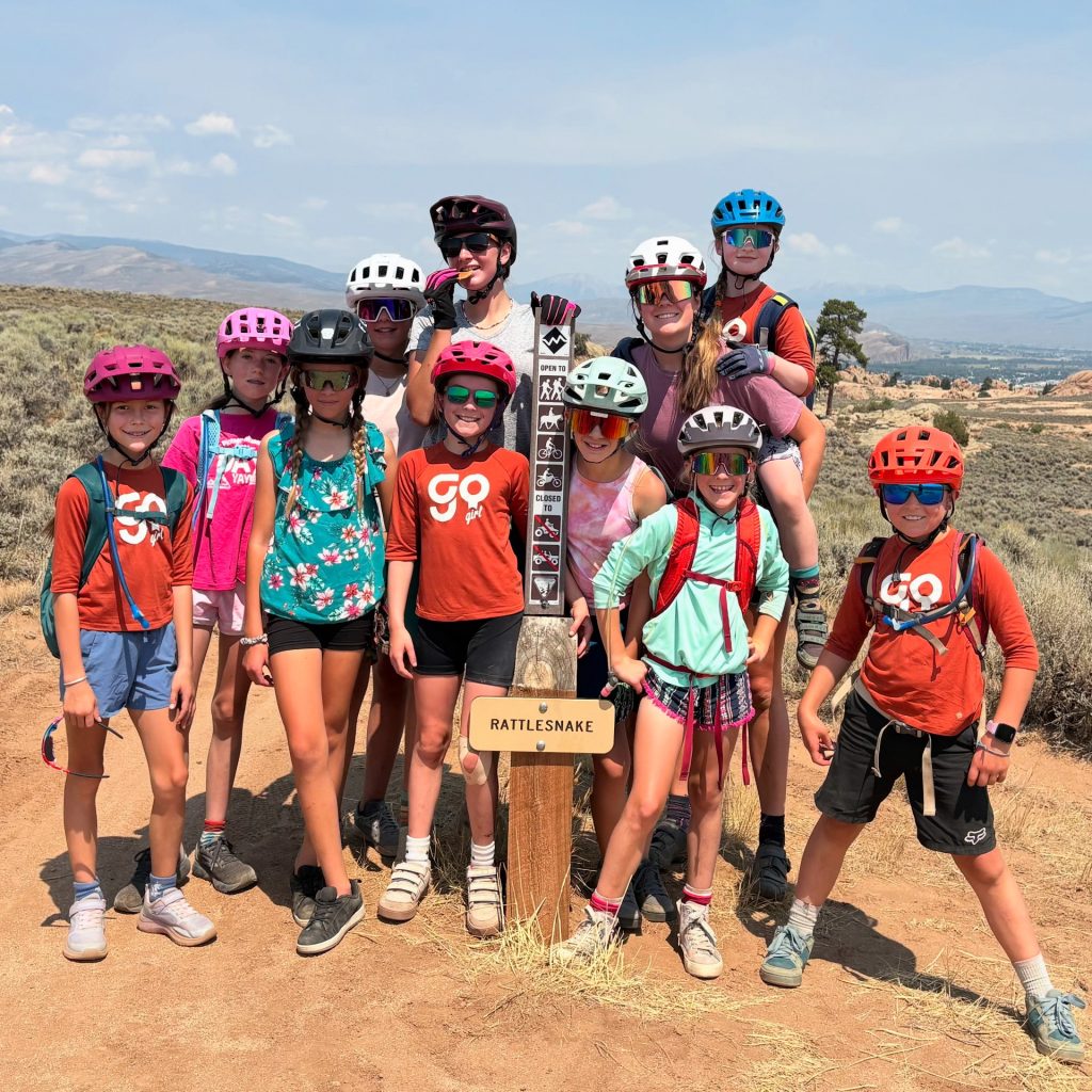 Nine Go Girl participants and two of their coaches stand around the Rattlesnake sign at Hartman Rocks.