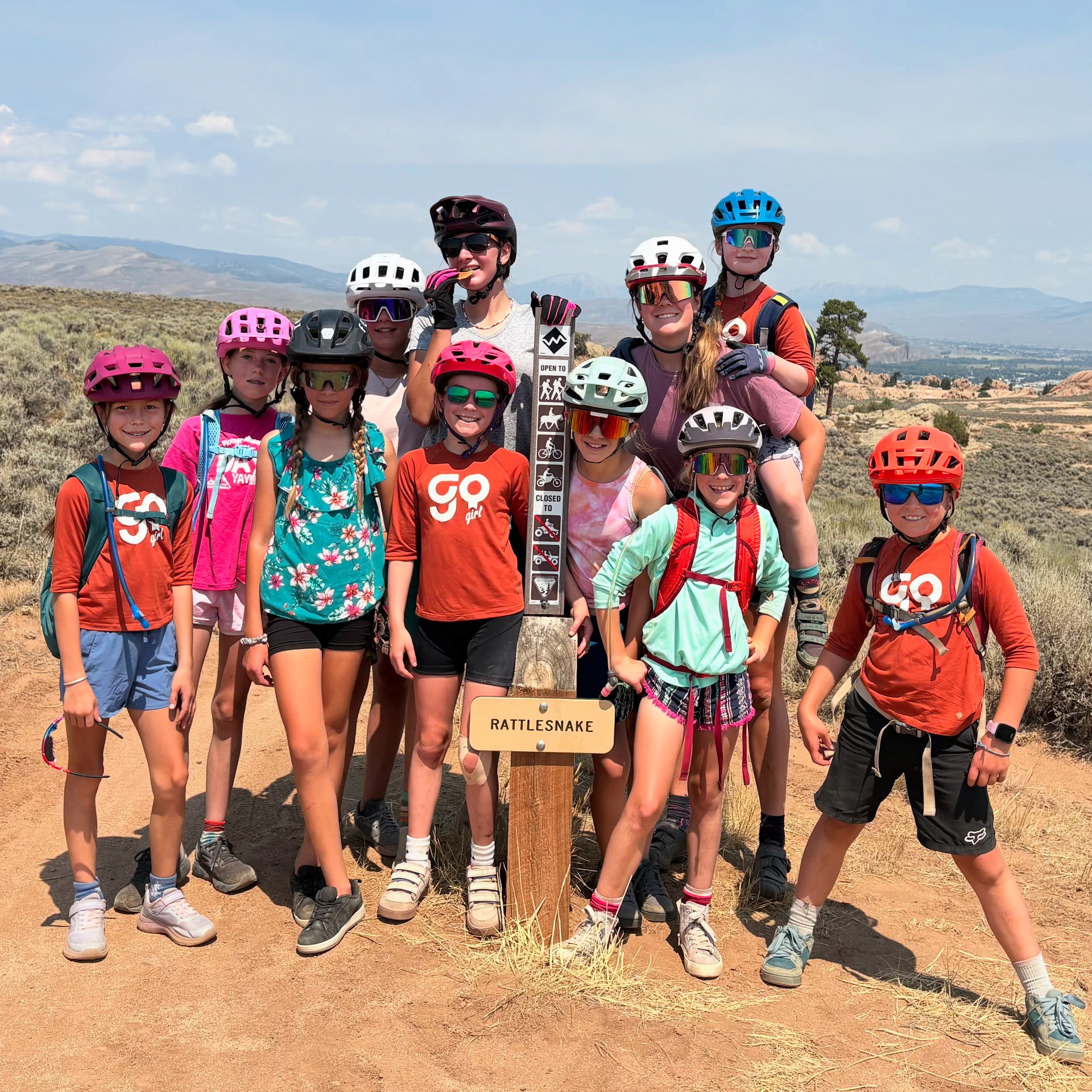 Nine Go Girl participants and two of their coaches stand around the Rattlesnake sign at Hartman Rocks.