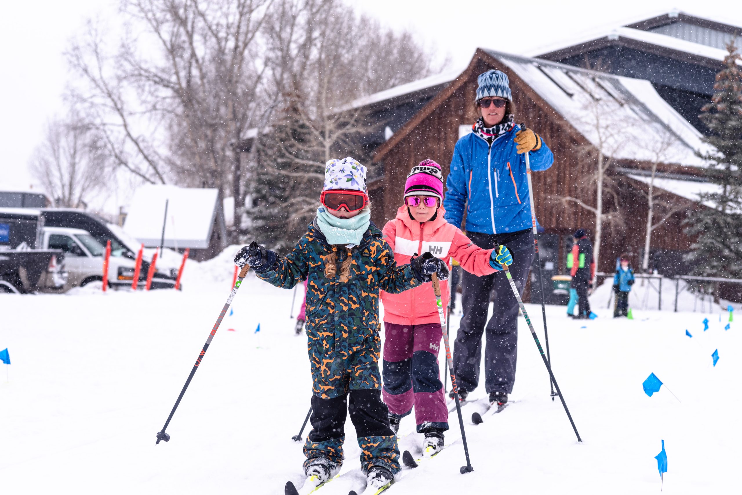 Two elementary-schoolers bundled up classic cross-country ski while an adult follows.