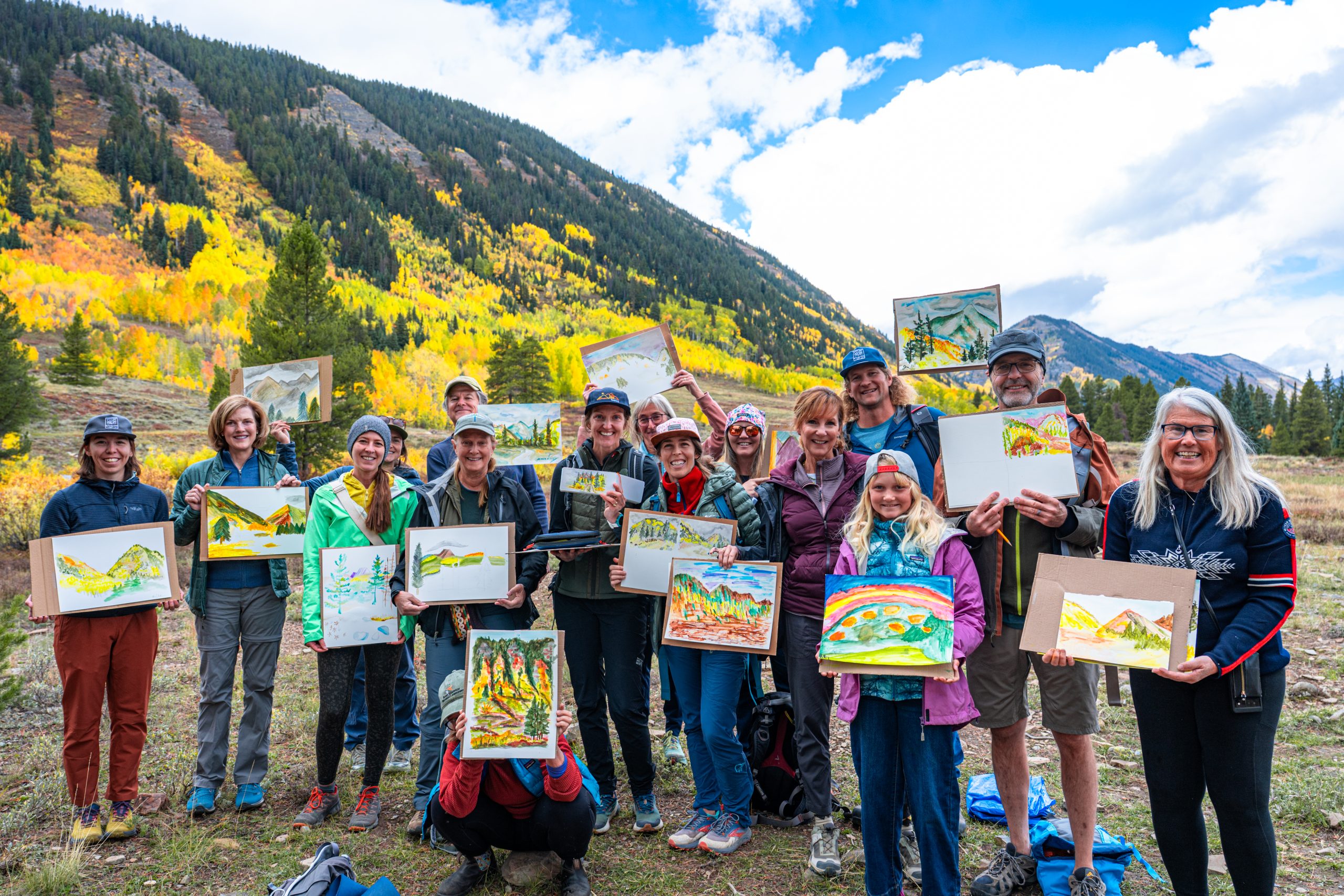 a group of hikers show off their watercolor paintings in front of a mountain
