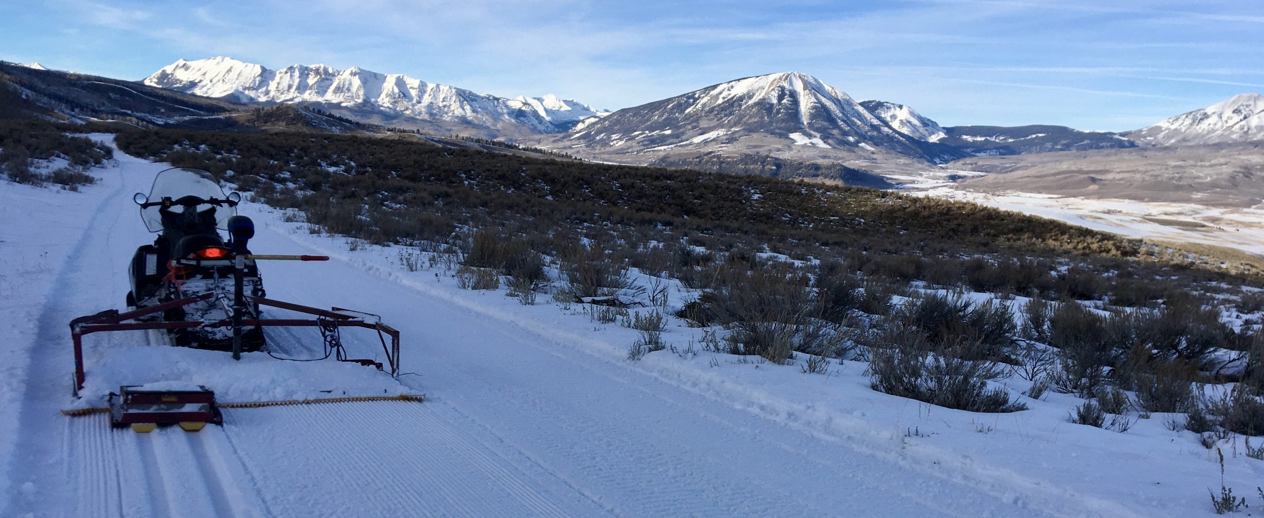 A snowmobile with a Nordic groomer & track setter sits in the foreground with the Anthracites and Carbon mountain in the background.