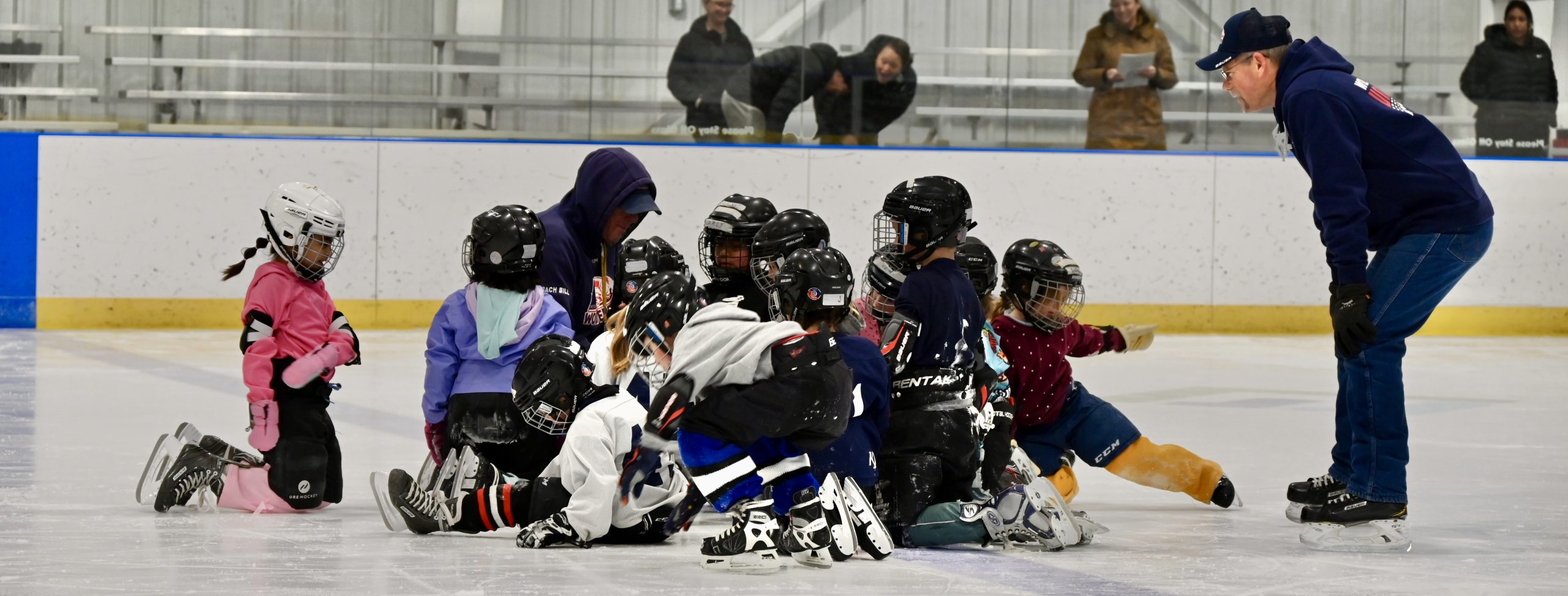 Skate for PE first graders decked out in hockey gear gather round their coach
