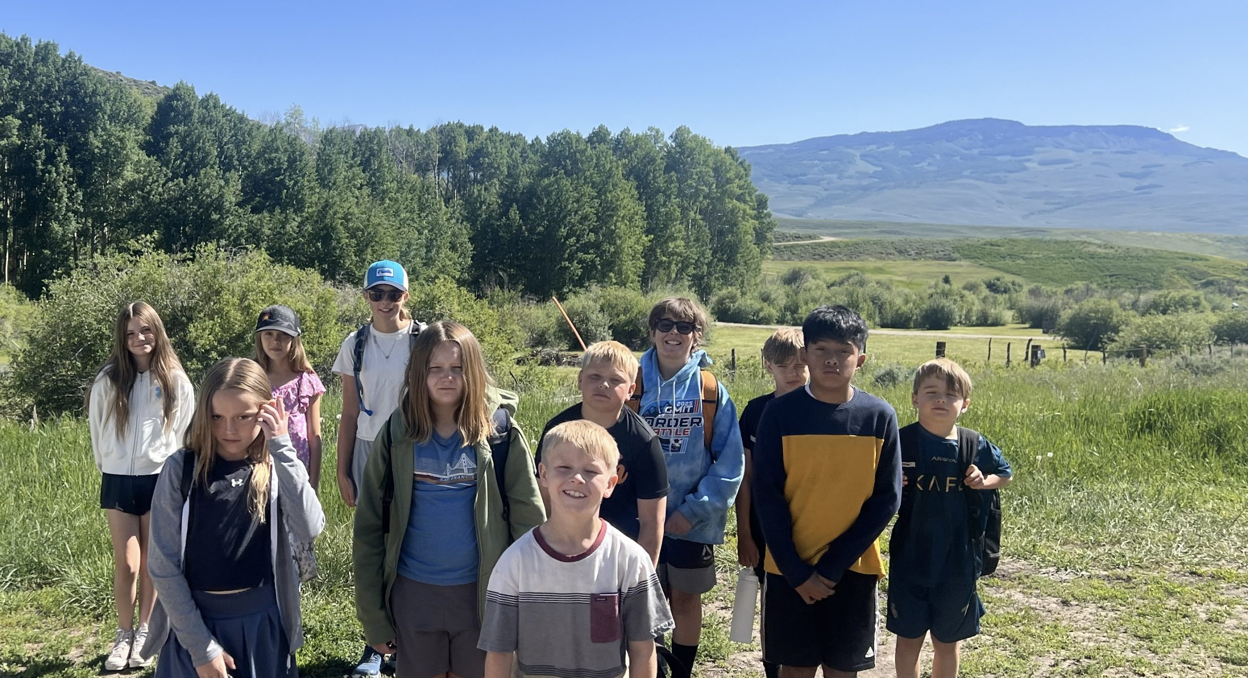 A group of student campers gather in front of a mountain.